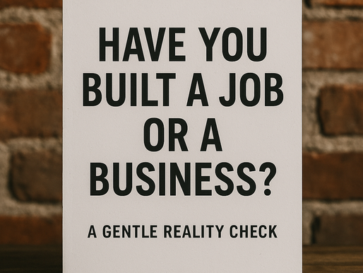 Sign on a wooden table reads: "Have you built a job or a business? A gentle reality check." Brick wall background. Text is bold and black.