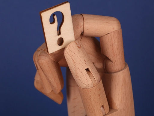 Wooden hand holding a small card with a cut-out question mark against a solid blue background, evoking curiosity and inquiry.