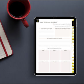 Tablet on a desk displaying "APRIL Focus Areas & Priorities" page. Nearby, a red cup of coffee and a notebook with a red spine.