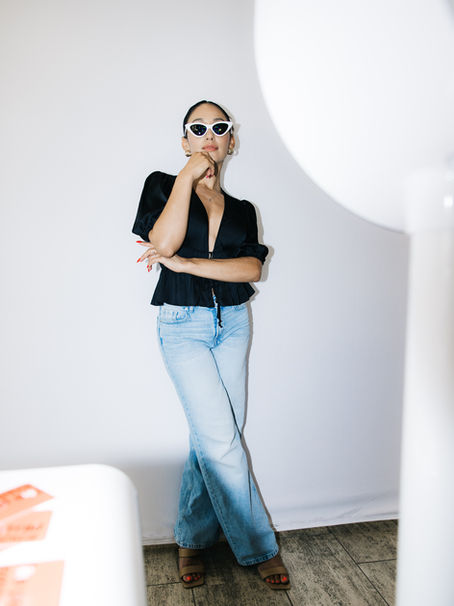 Stylish woman posing confidently in front of The Portrait Experience photo booth backdrop wearing white sunglasses, a black satin blouse, and light-wash jeans — modern DSLR photo booth setup in Coeur d’Alene for luxury events, weddings, and brand activations.