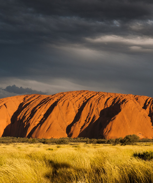 Uluru glowing red at sunset under a stormy sky
