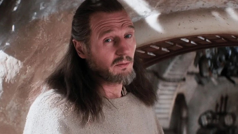 A man with long hair and a beard gazes intently in a rustic, shadowy room with curved walls, creating a thoughtful mood.