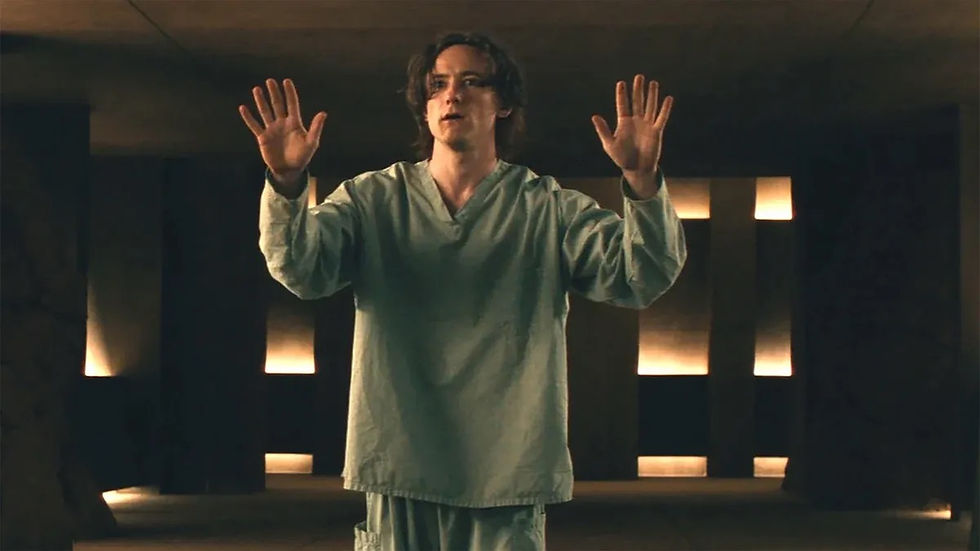 Bob in light scrubs with raised hands stands in a dim, modern room with glowing wall panels, conveying tension or apprehension.