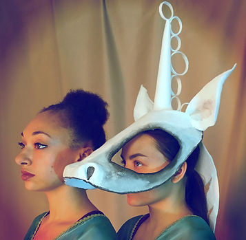 Close up of two performers looking left, one wearing a white mask inspired by the Ancient Minoan Genii