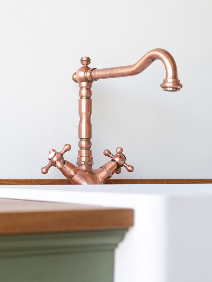 Detail van landelijke waterkraan boven een witte spoelbak in een massief houten dressoir
