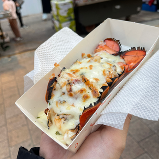 A Korean-style lobster topped with melted cheese and sauce, served in a paper tray at a street food 