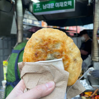a hot Korean street food pancake freshly fried, wrapped in paper, at a busy Seoul street market in a