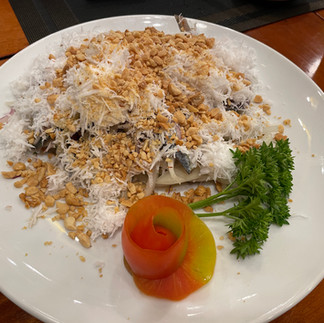 A plate of Vietnamese herring salad in Phu Quoc topped with shredded coconut, roasted peanuts, herbs, and vegetables.