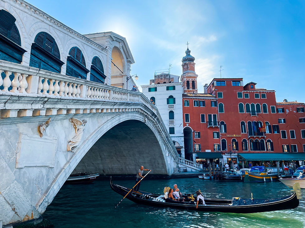 A gondola glides gracefully under the historic Rialto Bridge in Venice, surrounded by the vibrant architecture of the Grand Canal.
