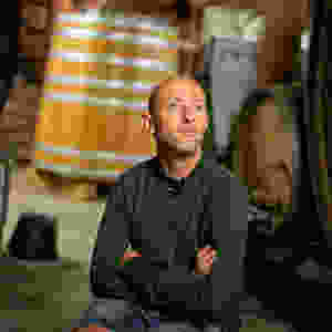 Le vigneron Christian Binner assis dans son chai bioclimatique, au milieu des foudres et tonneaux, en pull vert