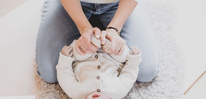 Woman sitting on the floor with a newborn baby between her legs demonstrates a baby massage