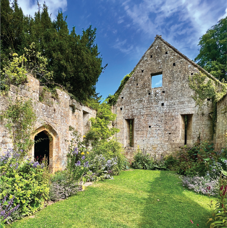 Ancient stone ruins at Sudeley Castle, partially covered in ivy, surrounded by green lawns and wildflowers.
