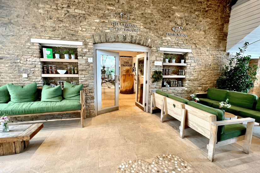 A beautifully designed farm shop with stone walls, wooden tables, and green cushioned seating, filled with organic products.