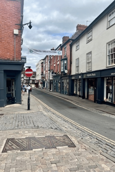 A quiet street in Ludlow with traditional British shopfronts and old architecture, set under a blue sky.