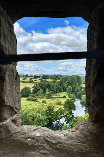 A scenic countryside view framed by a narrow stone window in Ludlow Castle’s walls.
