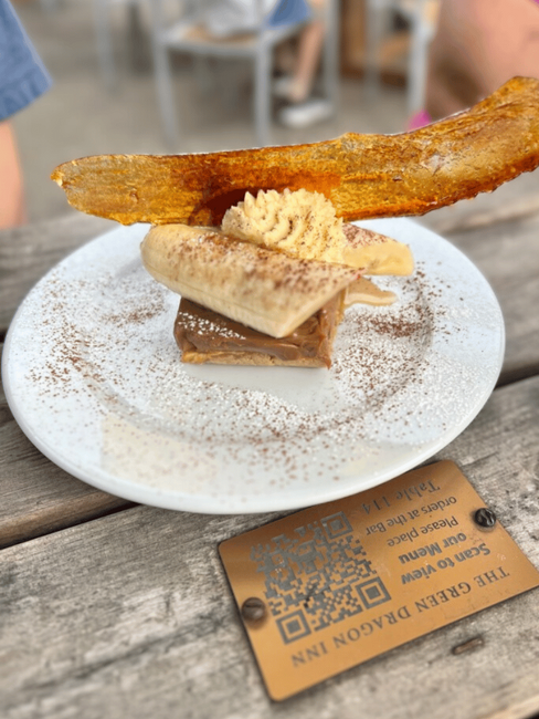 A beautifully plated banoffee dessert with layers of caramel, banana, and cream, topped with a caramelized sugar garnish, served on a rustic wooden table.