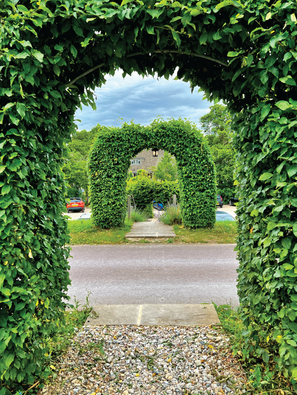 A symmetrical hedge archway leading to a picturesque view of Sudeley Castle’s gardens and driveway.