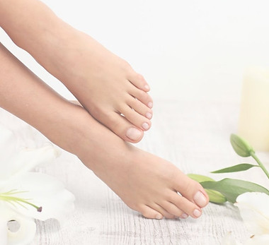 Mooie verzorgde damesvoeten met witte bloemen met groene blaadjes en drie witte kaarsen.