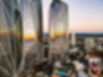 Aerial view of modern skyscrapers with reflective glass facades and geometric designs against a sunset sky.