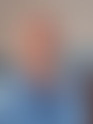 An elderly Caucasian man looking into the camera. Behind him are books authored by him.
