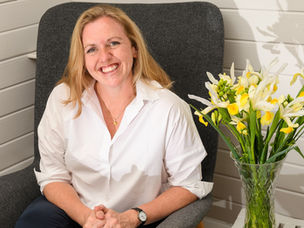 Nicola Ellwood, Executive Coach sat smiling next to some white and yellow flowers