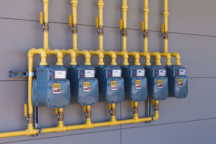 Row of residential natural gas meters and yellow pipe plumbing on exterior wall to measure