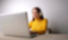 Woman in a yellow blouse on her laptop wearing headphones