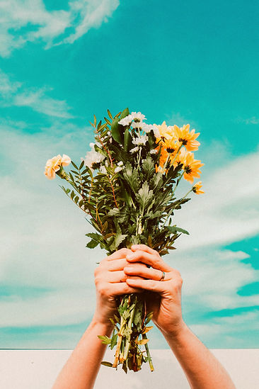 person holding bunch of yellow flowers up in the blue sky