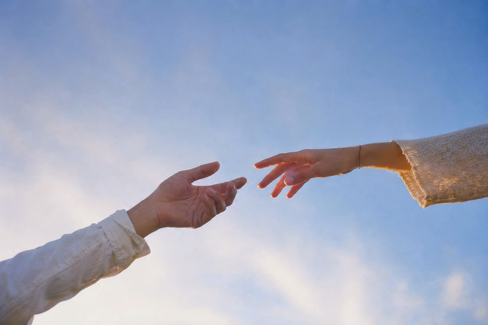 Two people’s hands reaching toward each other against a bright blue sky, suggesting connection and tenderness.