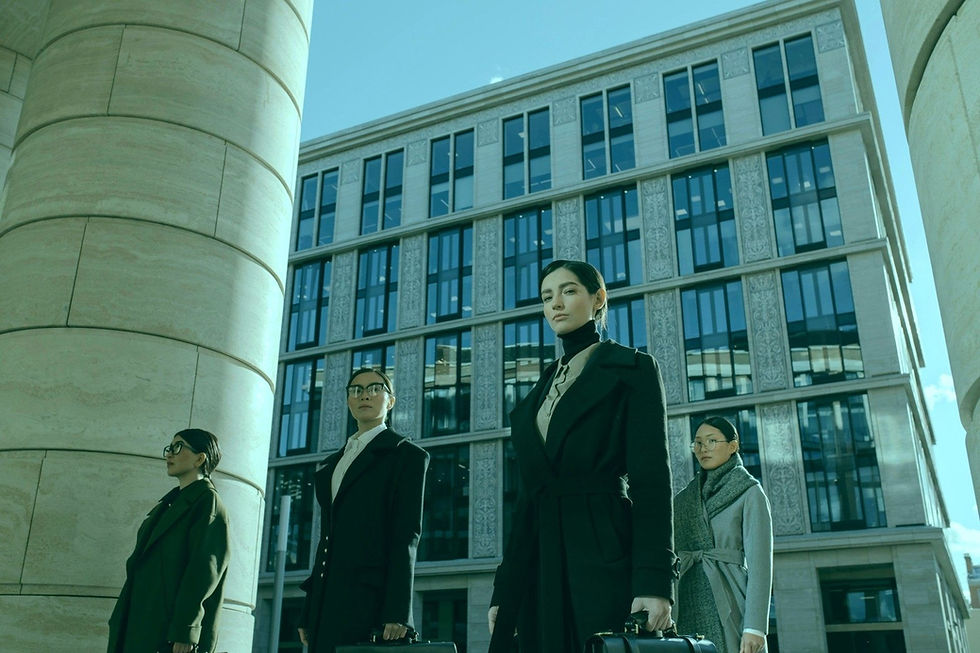 Four businesswomen in dark coats stand before a modern office building, looking serious and confident.