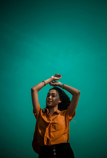 Woman in orange shirt, arms raised, teal background