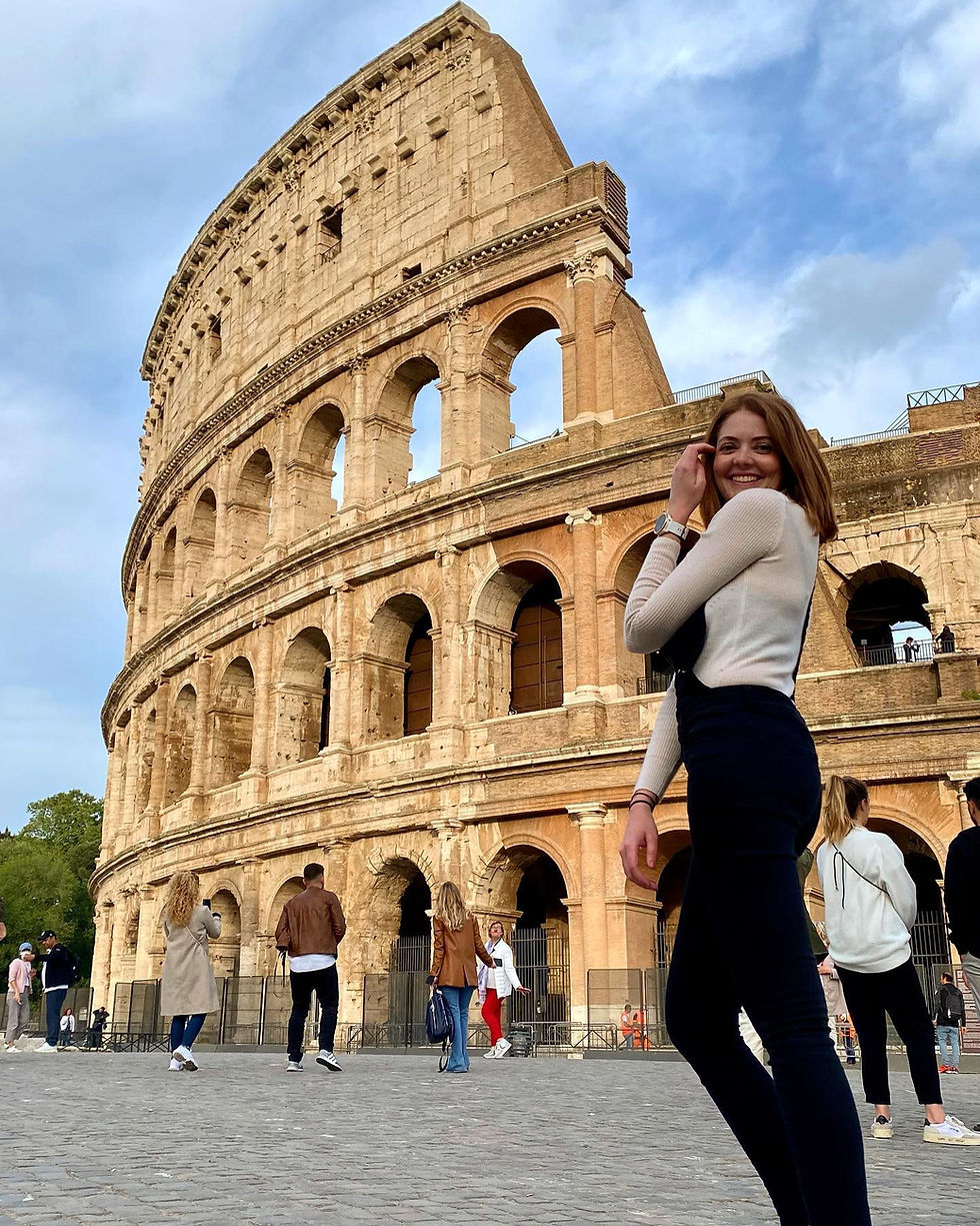 Female in Rome at the Colosseum wearing a white top and black dungarees.
