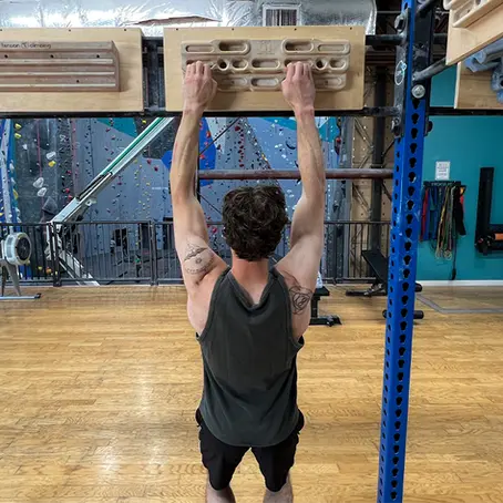 A climber hangs off of a hangboard. A hangboard is a rock climbing training tool with multiple grips to train for different terrains.