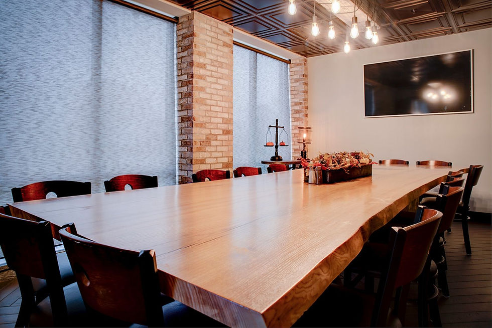 Large wooden table with chairs in a room with brick walls and hanging lights. A centerpiece with autumn decor, closed blinds, and a TV. Conference Room.