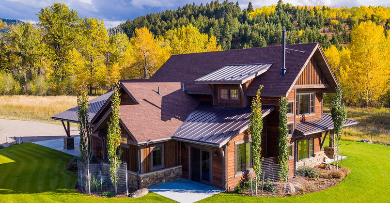 Large Montana home with brown metal roofing, wood-and-stone exterior, and landscaped yard.