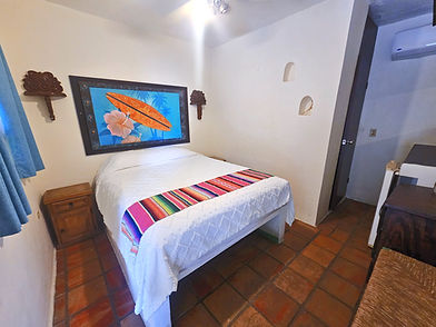 Cozy Cabo Inn Hotel room: white bed, colorful blanket, surfboard art