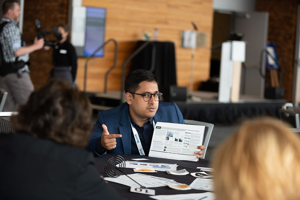 Three people sit at a table with scattered papers during the BlueTech Forum event in Vancouver, BC.