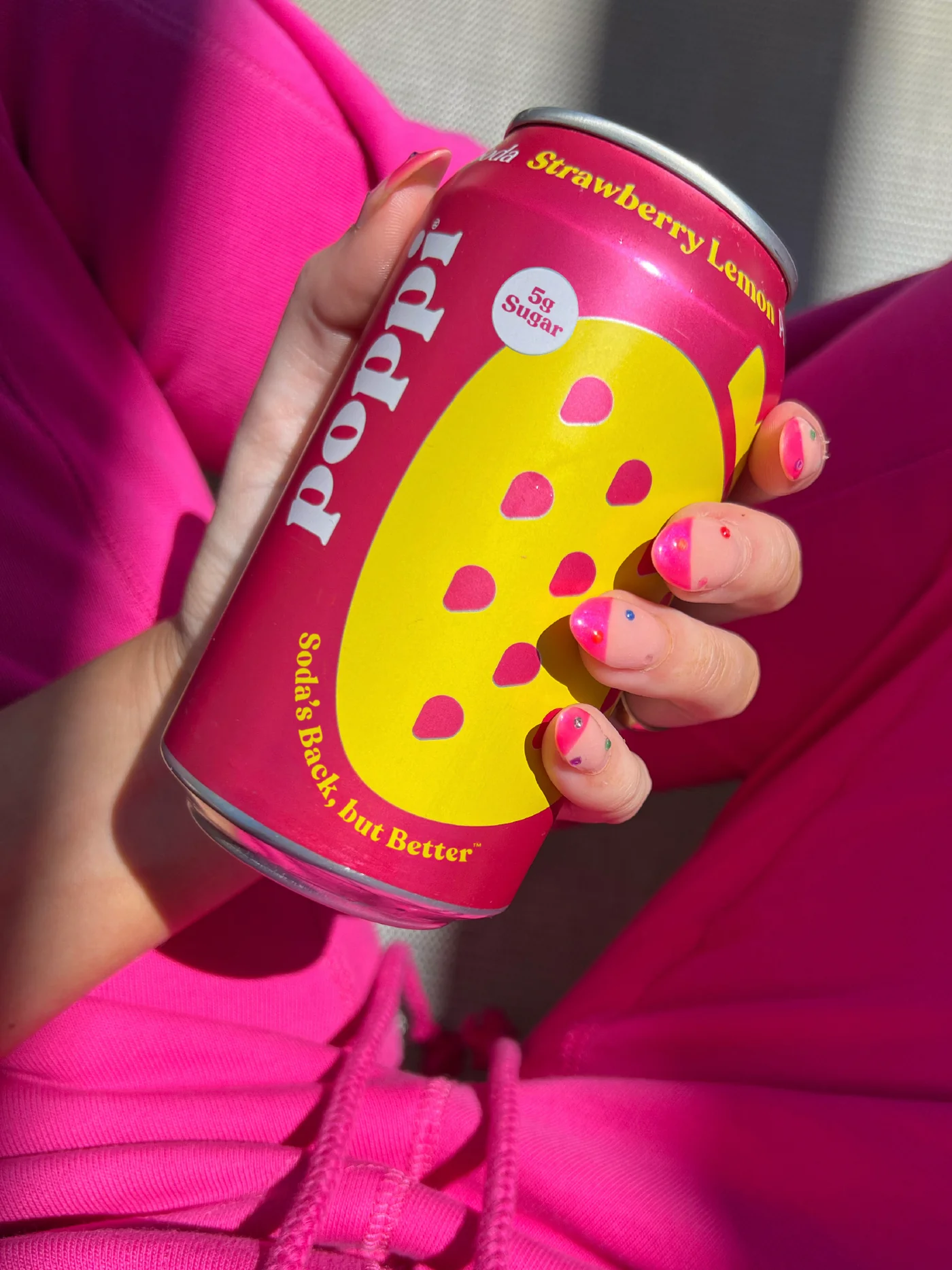 Strawberry Lemon Poppi Ad with hands holding a bright pink and yellow can