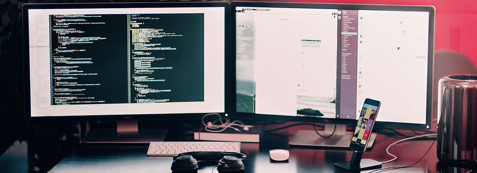 two computer monitors on desk with headphones, keyboard and phone.