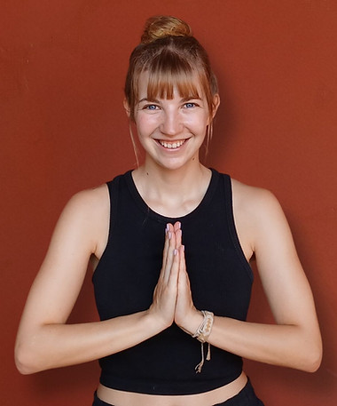 Bild von Tamara mit gefalteten Yoga Händen mit rotem Hintergrund