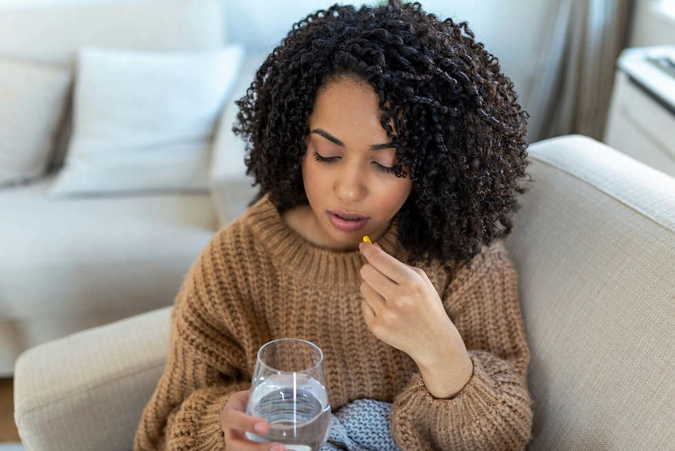 Woman in a brown sweater holding a pill and a glass of water.