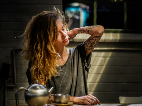 woman with tattoos making tea and looking stressed.
