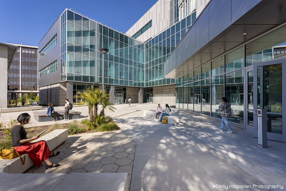 Students relax and walk in a sunny modern glass campus courtyard with benches, palm plants, and clear blue sky; Emily Hagopian Photography