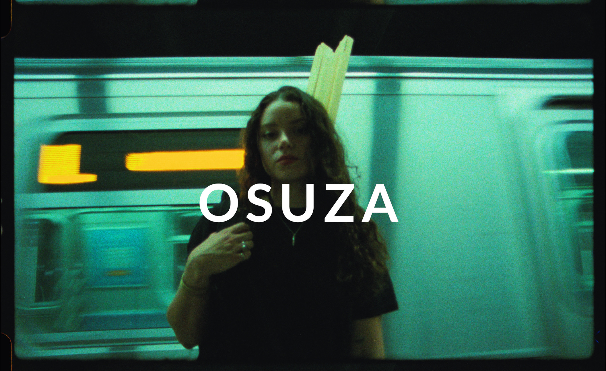 a young woman on a subway platform wearing an Osuza design backpack. The Osuza brand logo is featured over her. 