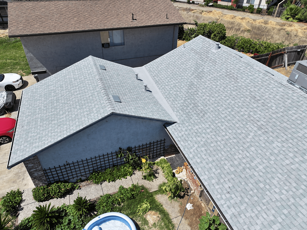 Aerial view of two gray houses with shingled roofs, green garden below, and a backyard pool. Sunny day, clear sky.
