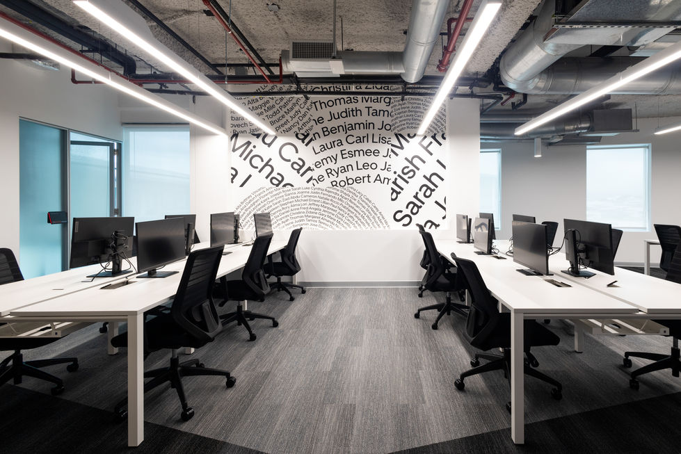 Modern office space with desks, computers, and a wall of names. Casalvolone Arquitectura.