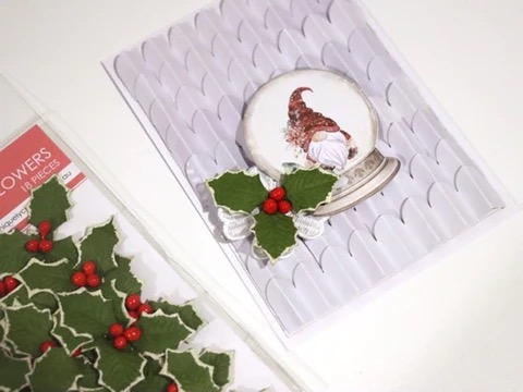 card showing the layered scalloped paper background on card front with snowglobe creative cut with christmas holly layered on a lace flower