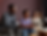 Three people sit on a couch, engaged in conversation. One gestures with hands. Background is a room with brown walls. Mood is thoughtful.