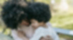 A woman embraces a child on a park bench. Both have curly hair. The background is green and leafy, creating a serene, comforting mood.