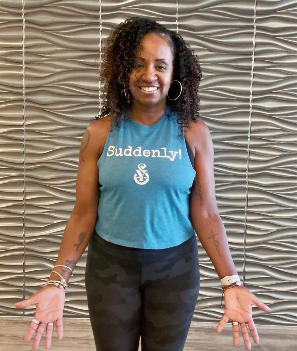 Courtenay Brown wearing a “Suddenly” T-shirt at Shabach Yoga, symbolizing faith, courage, and transformation.